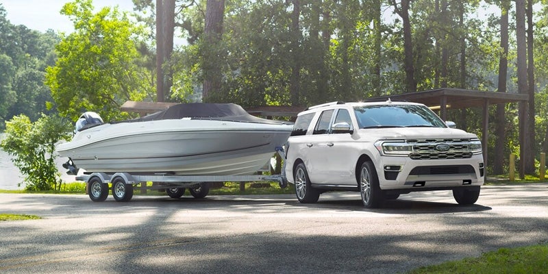 An all new 2024 White Ford Expedition towing a boat next to a body of water. - Jack Madden Ford Norwood, MA