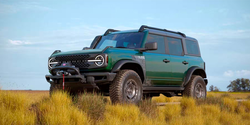 An all-new green Ford Bronco parked in a tall grass field. - Jack Madden Ford Norwood, MA
