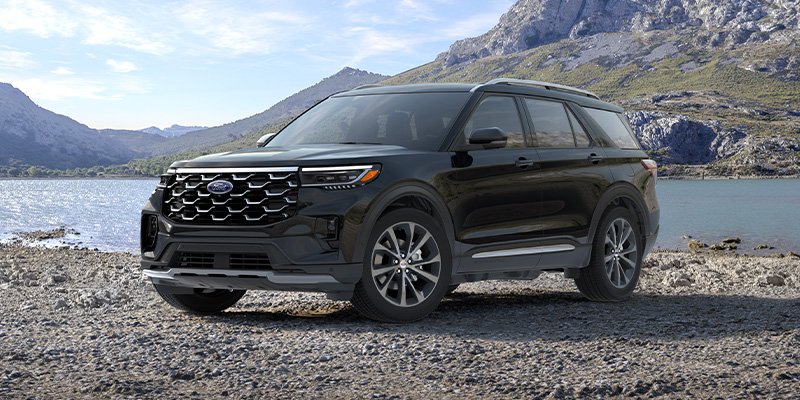 An all-new black 2025 Ford Explorer parked on a rocky beach in front of a stream and mountains. - Jack Madden Ford Norwood, MA